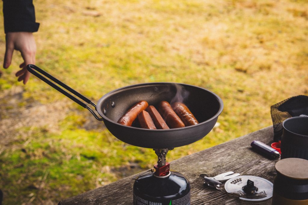Hotdogs being cooked in a pan over a camp stove