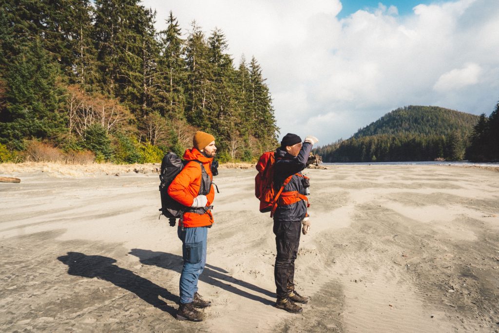 Two people standing on a sandy beach with hiking gear on